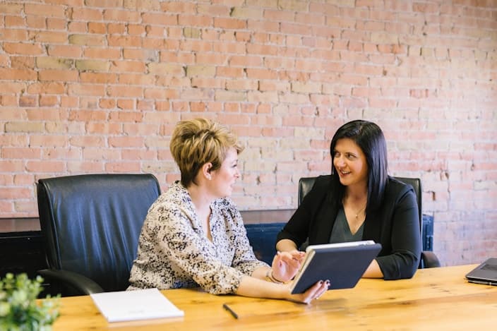 Two colleagues discussing work on a tablet at a wooden desk